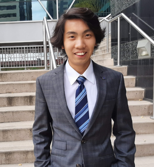 henry tsang posing in business attire in front of stairs, near james short park calgary with skyscrapers in the background